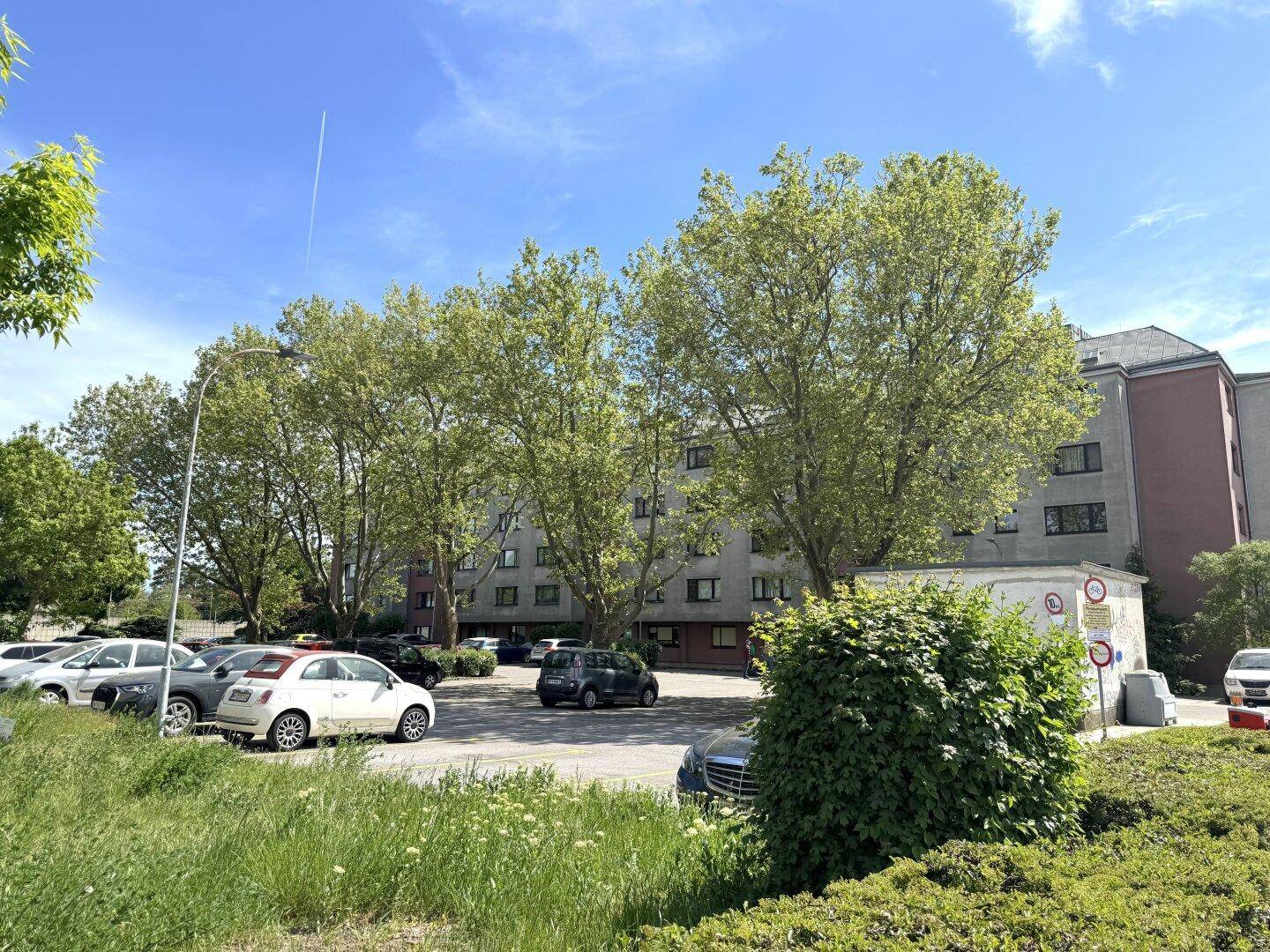 Weitläufiger Außenparkplatz mit vielen Autos, umgeben von Bäumen und Wohngebäuden.