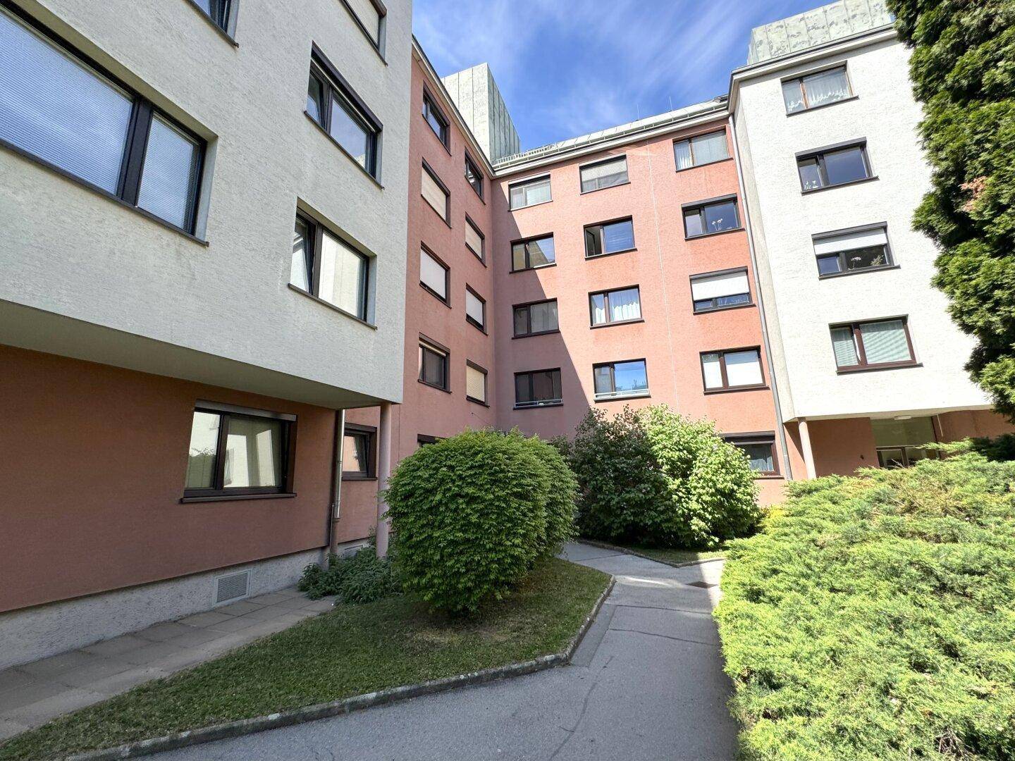 Außenansicht von Wohngebäuden mit farbigen Fassaden und grünen Büschen im Vordergrund.