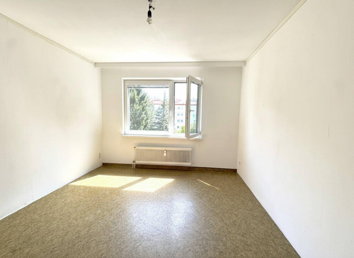 Leeres Zimmer mit Linoleumboden, weißen Wänden und einem Fenster, das viel Licht hereinlässt.