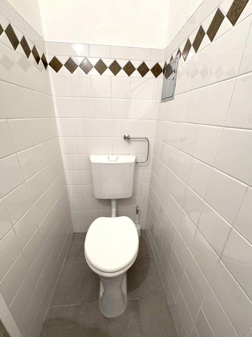 Kleines WC mit Toilette, weißen Fliesen und einer dekorativen Bordüre.