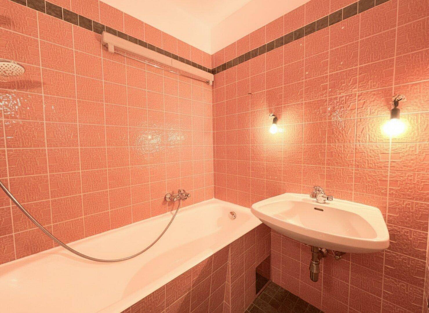 Badezimmer mit rosa-orangen Fliesen, einer Badewanne mit Duschfunktion und einem Waschbecken.