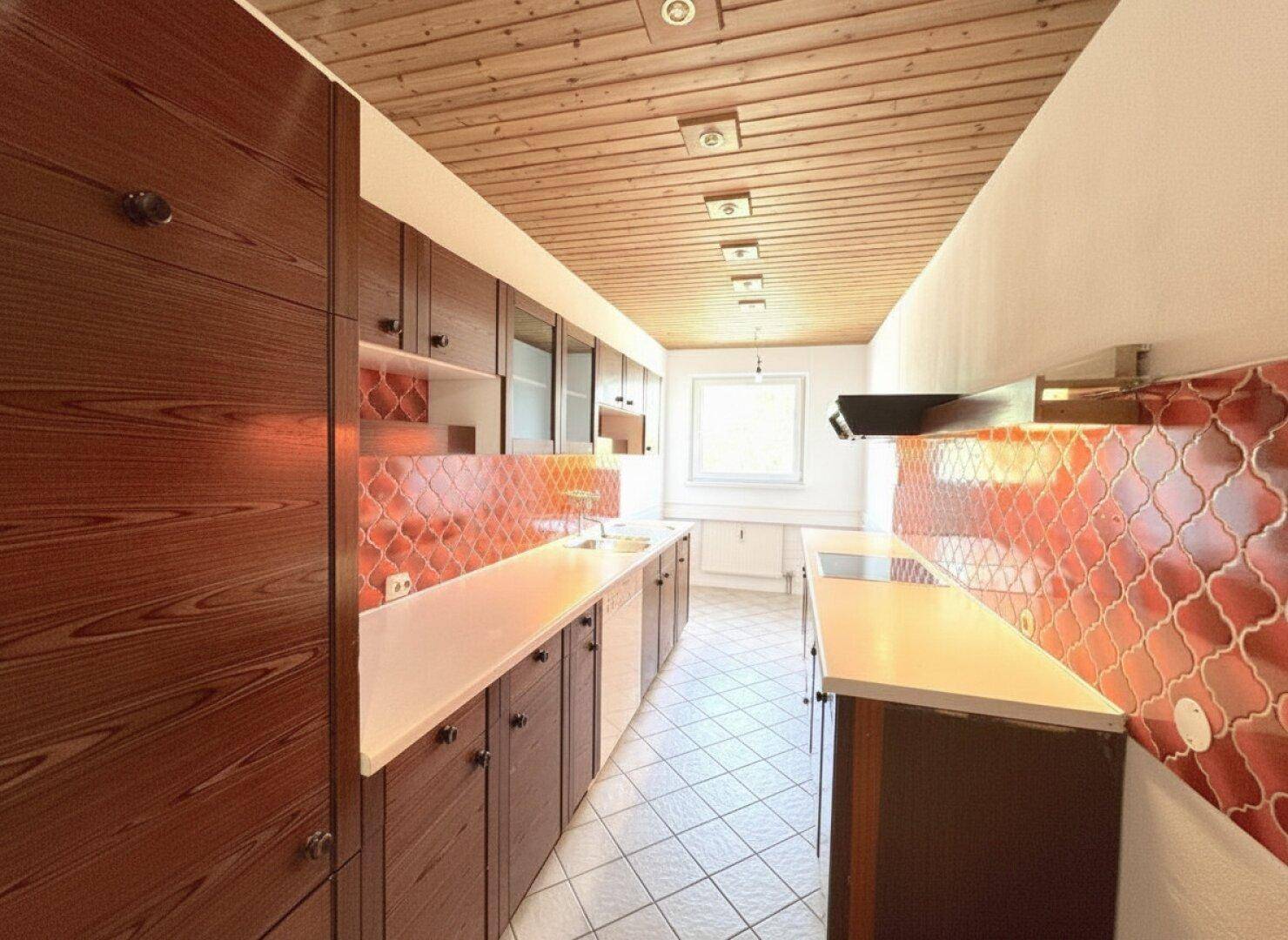 Schmale Küche mit Holzschränken, weißen Arbeitsplatten und auffälligen orangefarbenen Fliesen.