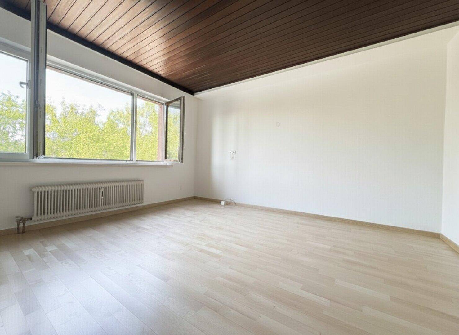 Geräumiges, leeres Zimmer mit Holzboden, weißen Wänden und einer Holzdecke.