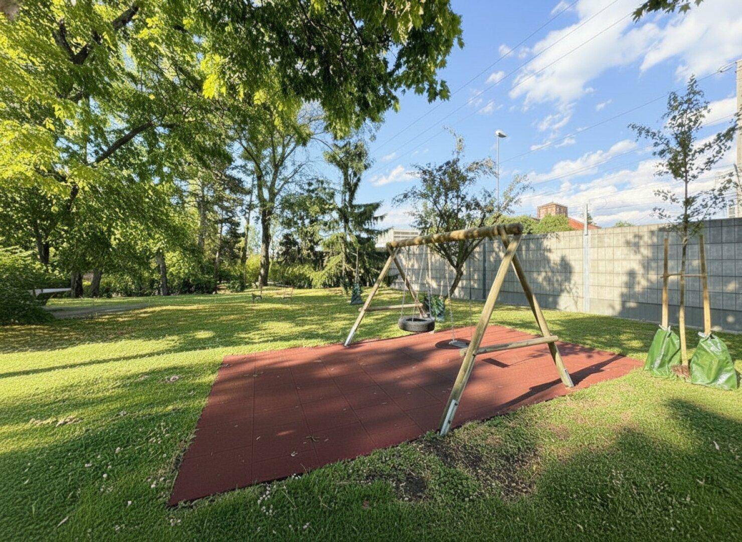 Grüner Gartenbereich mit einem Schaukelgerüst und weicher Fallschutzmatte für Kinder.