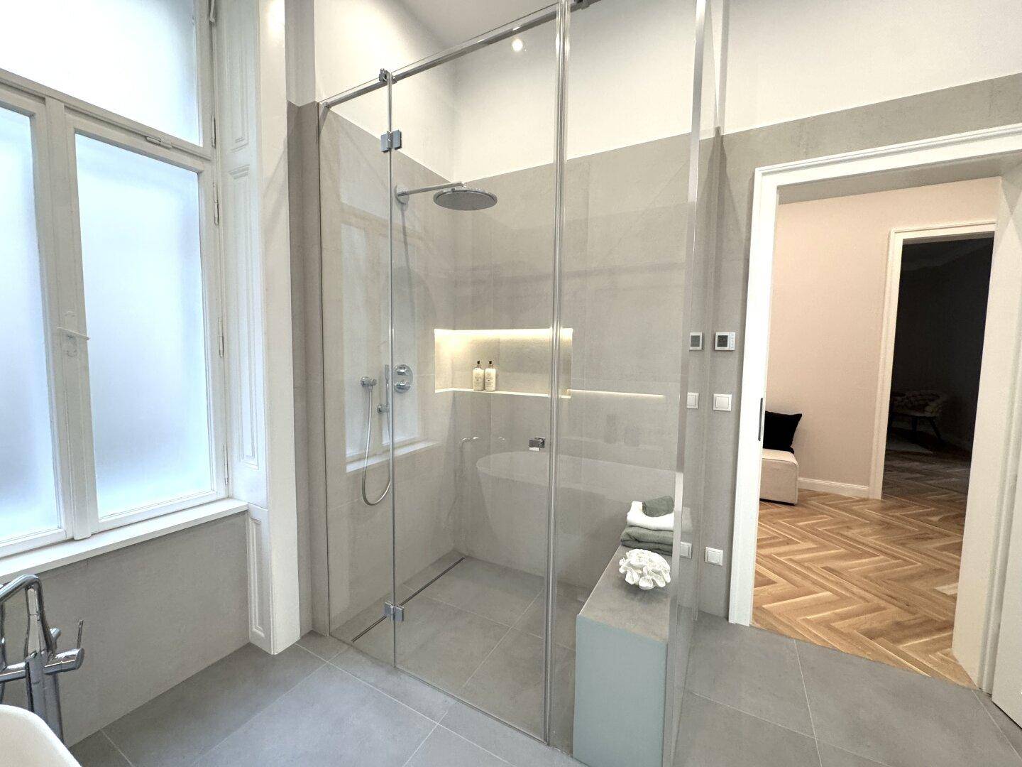 Geräumige begehbare Dusche mit Regenduschkopf und Blick auf die freistehende Badewanne.
