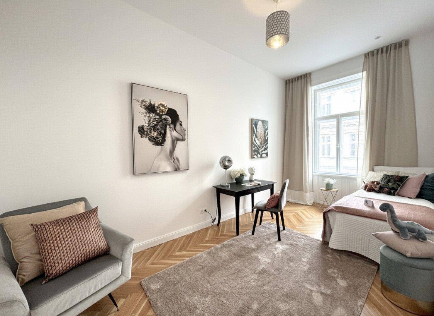 Helles Schlafzimmer mit Fischgrätparkett, einem großen Fenster und einem kleinen Schreibtischbereich.