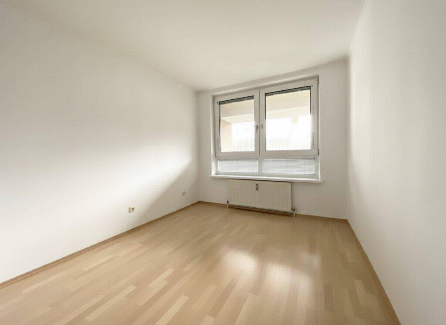 Leeres Zimmer mit hellem Holzboden und Fenster, bietet vielseitige Nutzungsmöglichkeiten.