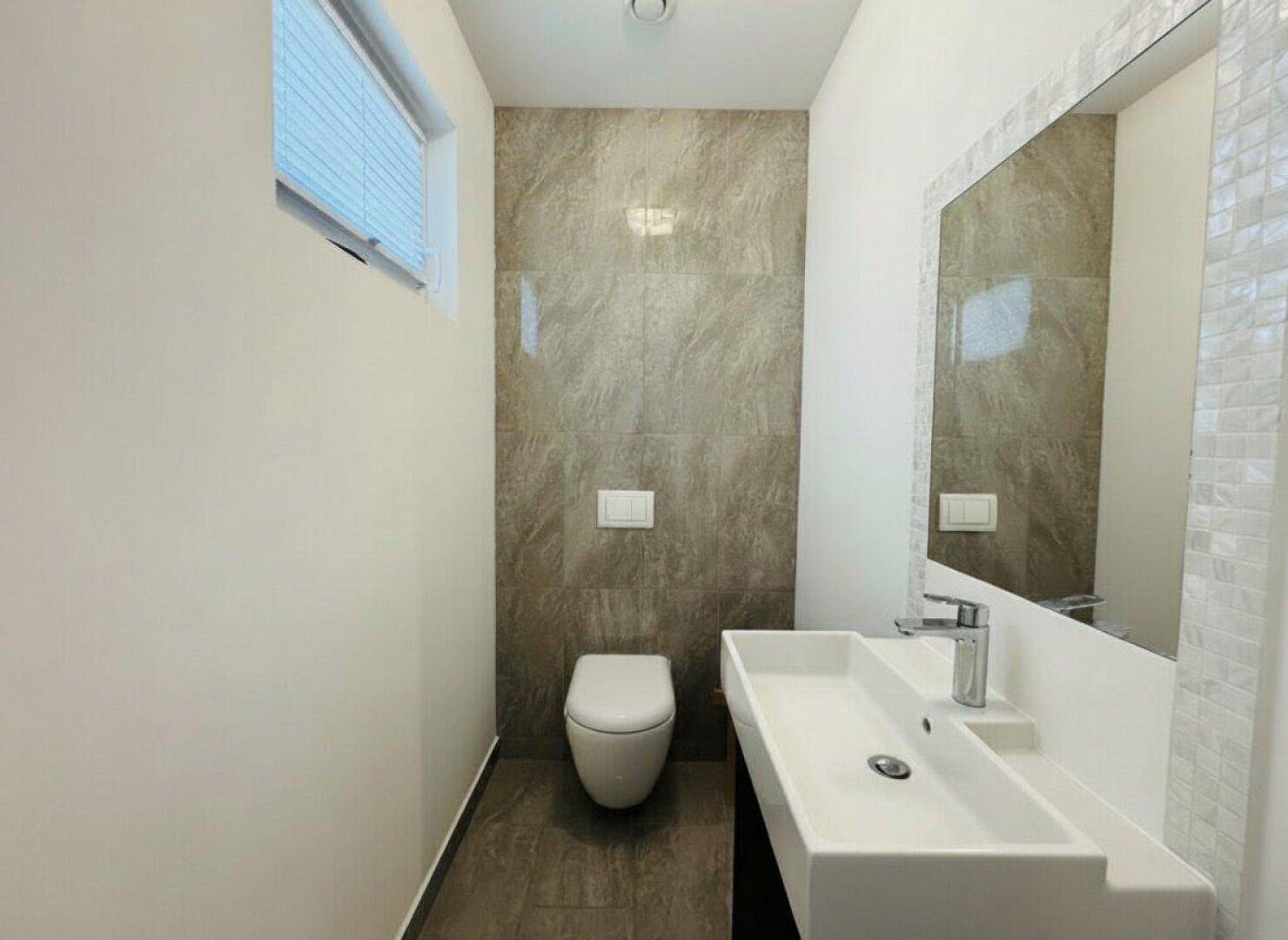 Modernes Gäste-WC mit Wand-WC, stilvollem Waschbecken und großformatigen Fliesen.