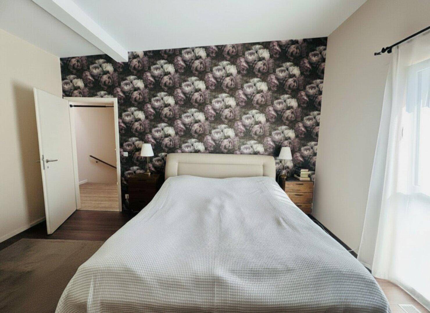 Schlafzimmer mit auffälliger floraler Tapete an einer Wand und dunklem Holzboden.