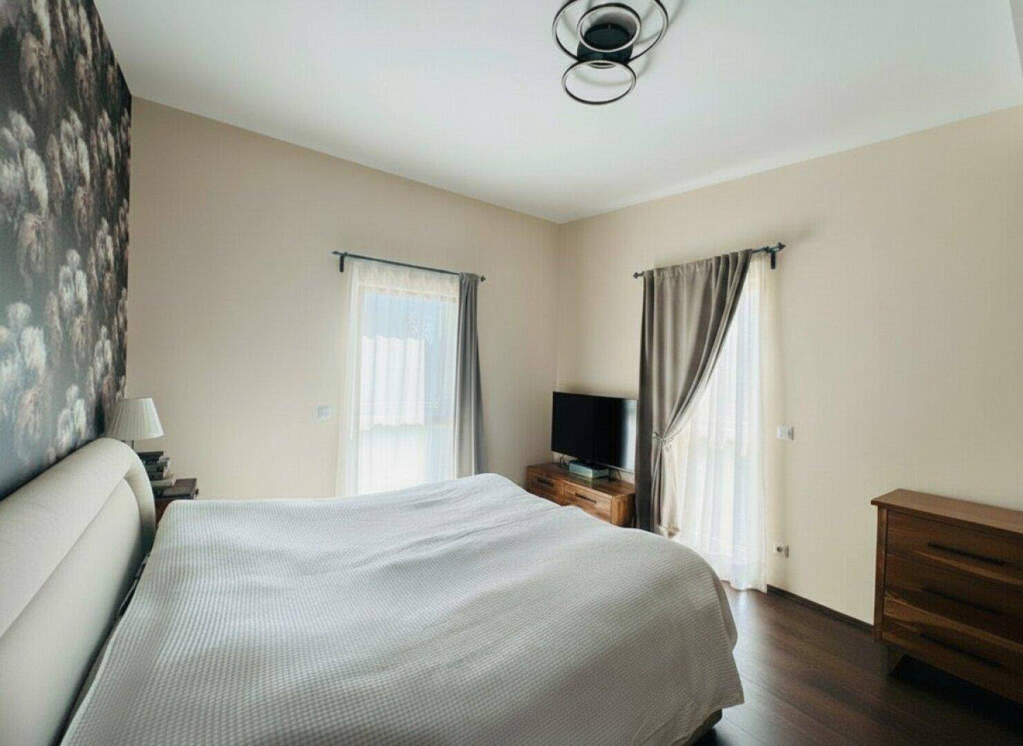 Gemütliches Schlafzimmer mit Doppelbett, dunklem Holzboden und zwei Fenstern.