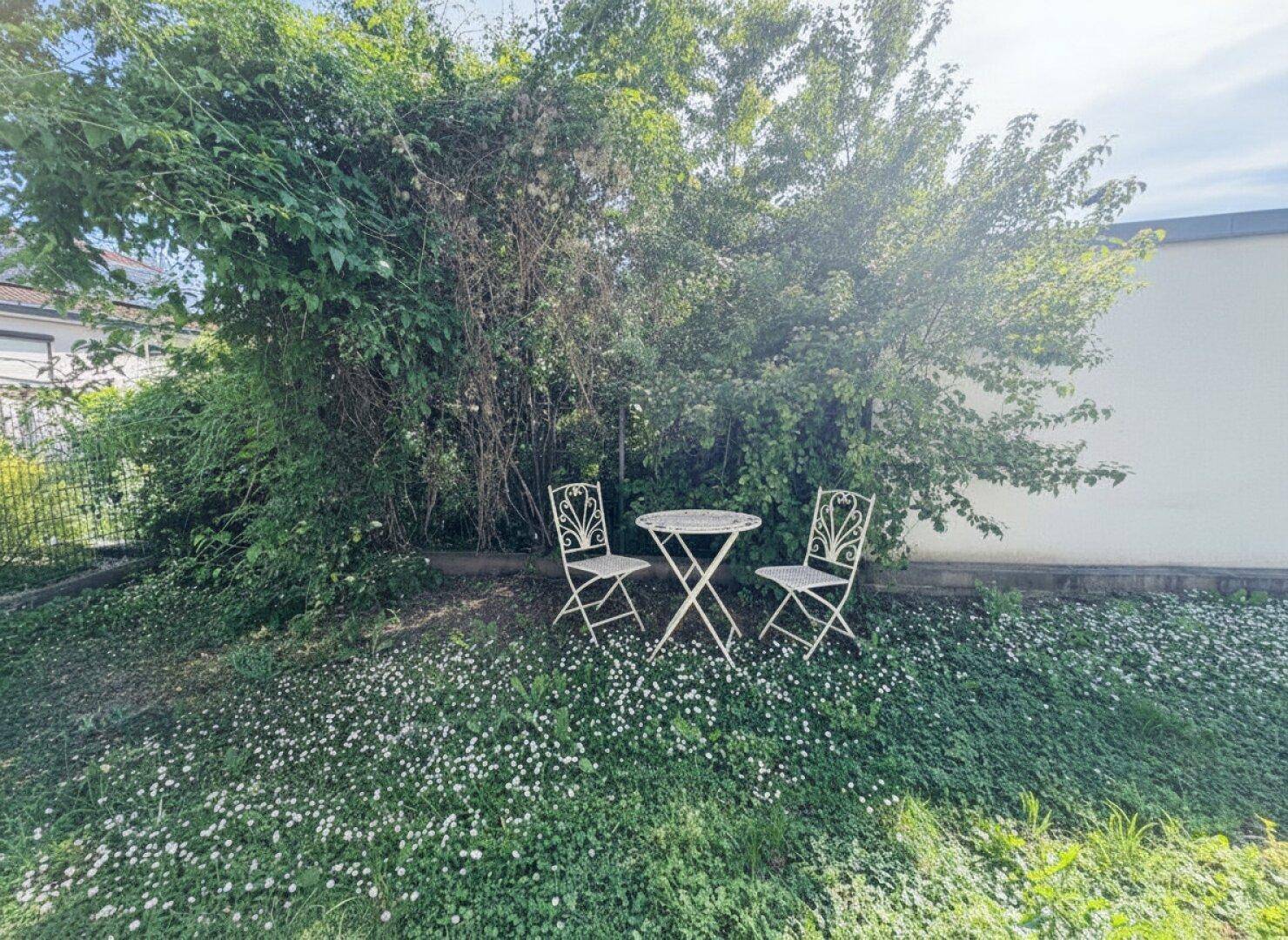 Gemütliche Sitzecke im grünen Garten, umgeben von üppiger Vegetation und Blumen.