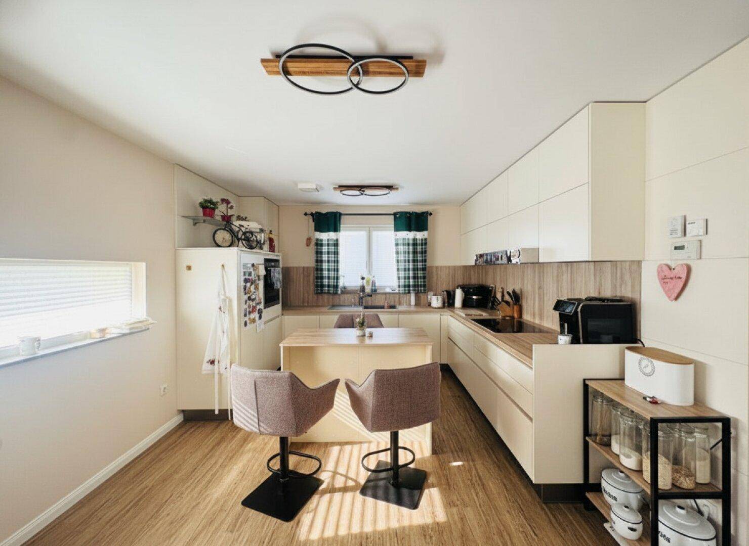Moderne Küche mit hellen Schränken, Holzdetails und einer zentralen Kochinsel mit Barhockern.