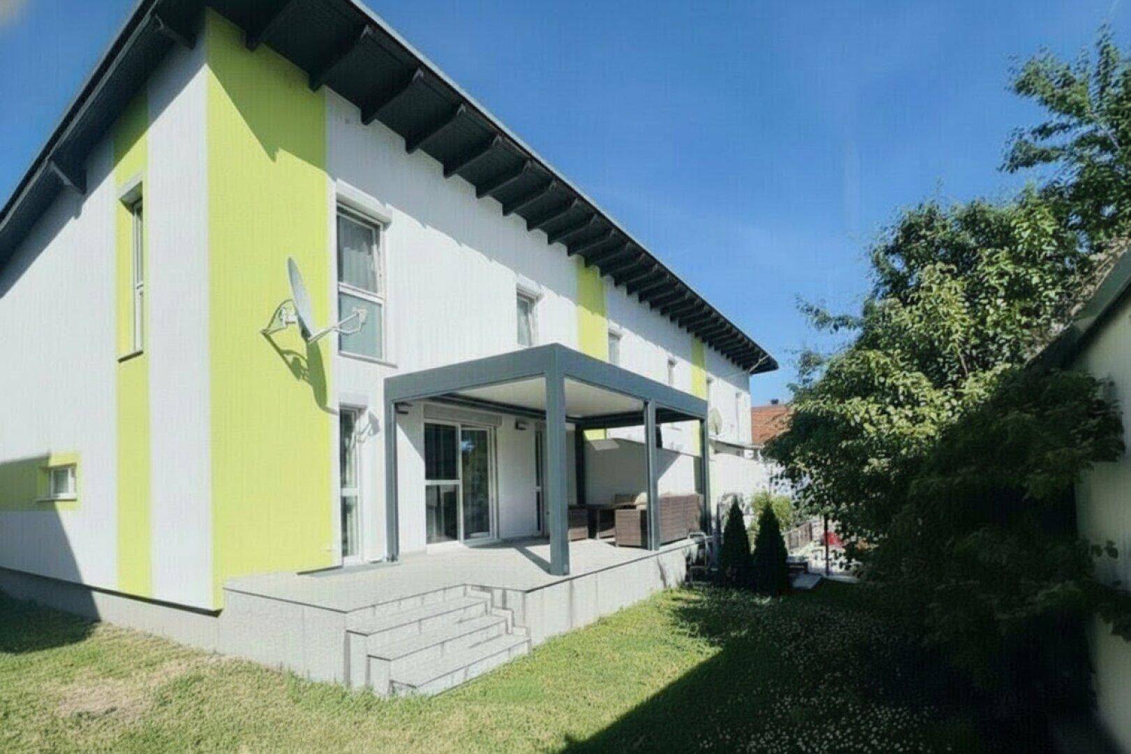 Modernes Reihenhaus mit weiß-grüner Fassade und überdachter Terrasse im Gartenbereich.