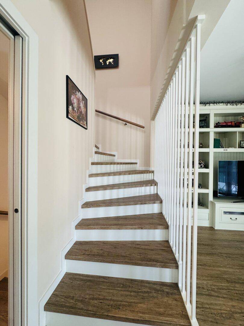Moderne Treppe mit Holzstufen und weißem Geländer, die zu den oberen Stockwerken führt.