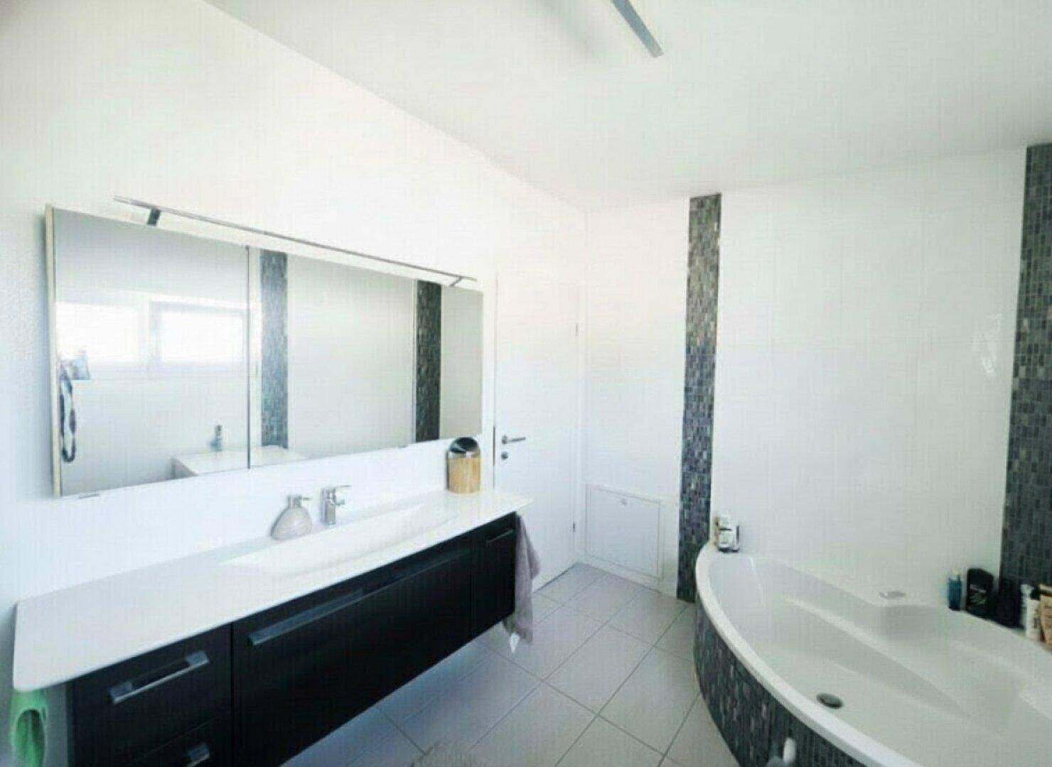Modernes Badezimmer mit Badewanne, großem Spiegel und dunklem Waschtischunterschrank.