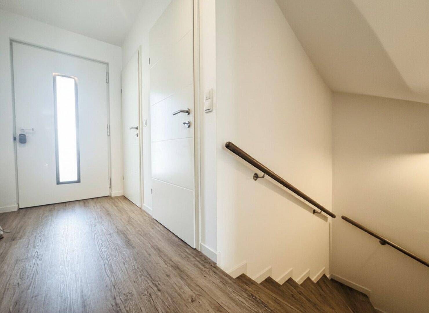 Heller Eingangsbereich mit moderner Haustür und Laminatboden, der zu den Innenräumen führt.