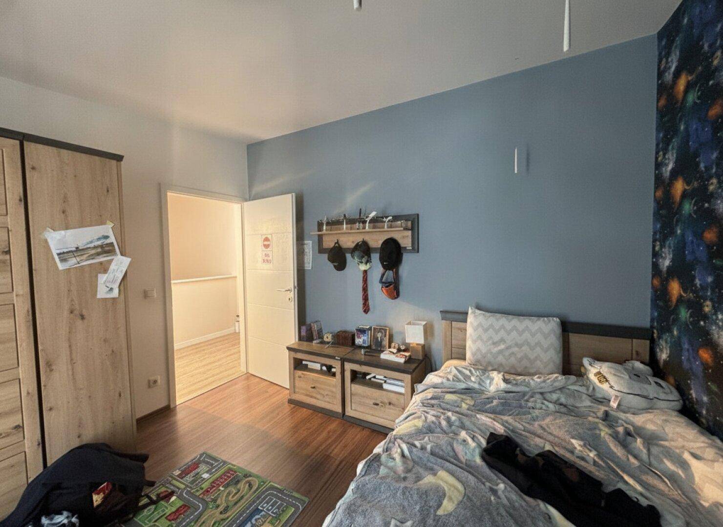 Helles Kinderzimmer mit Holzboden, Kleiderschrank und Zugang zum Flur.