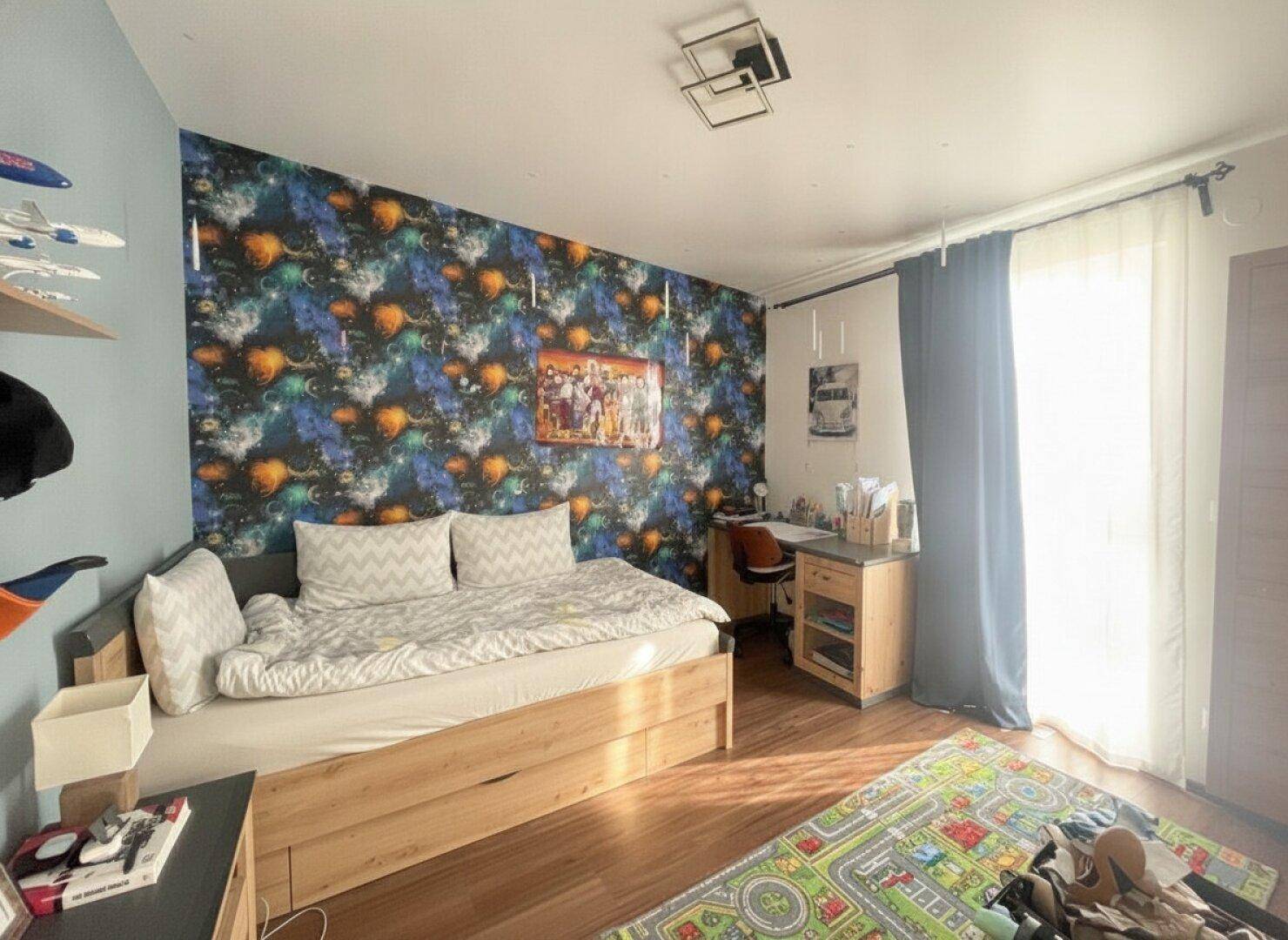 Kinderzimmer mit farbenfroher Tapete, Holzboden und viel Tageslicht.
