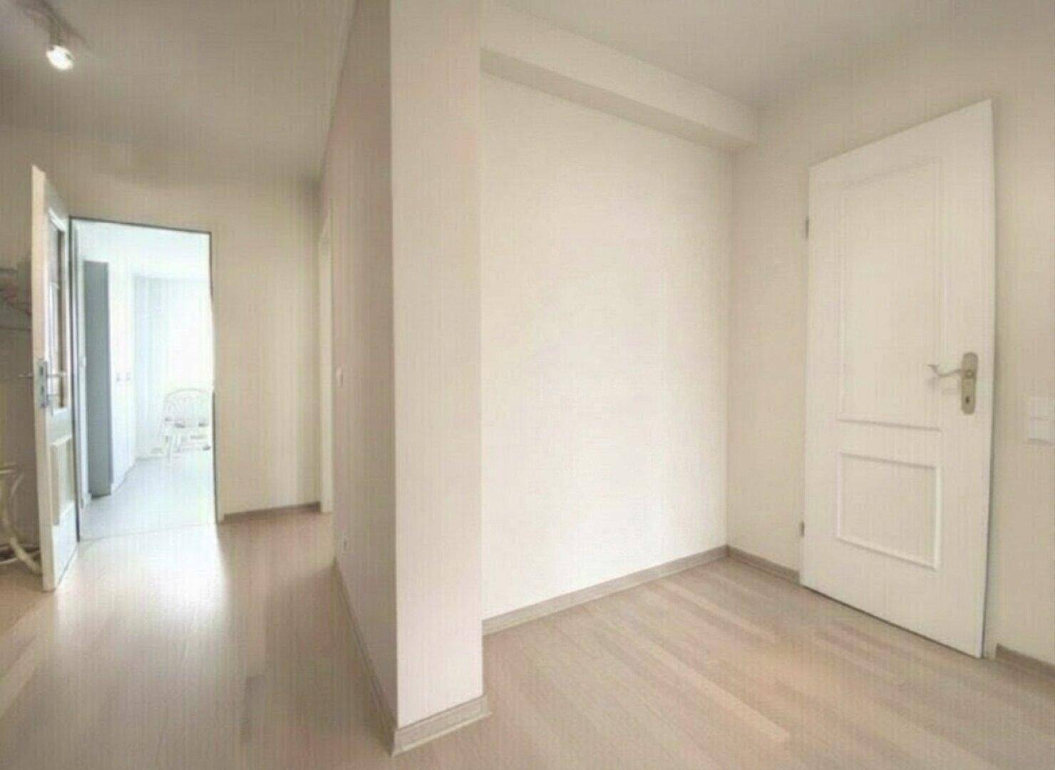 Heller Flur mit Holzboden und weißer Tür, der zu weiteren Räumen der Wohnung führt.