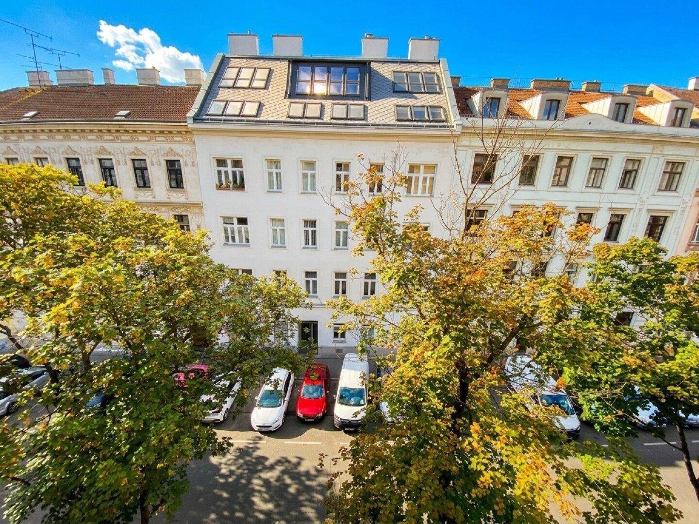 Gebäudeansicht von oben mit Bäumen und parkenden Autos auf der Straße.