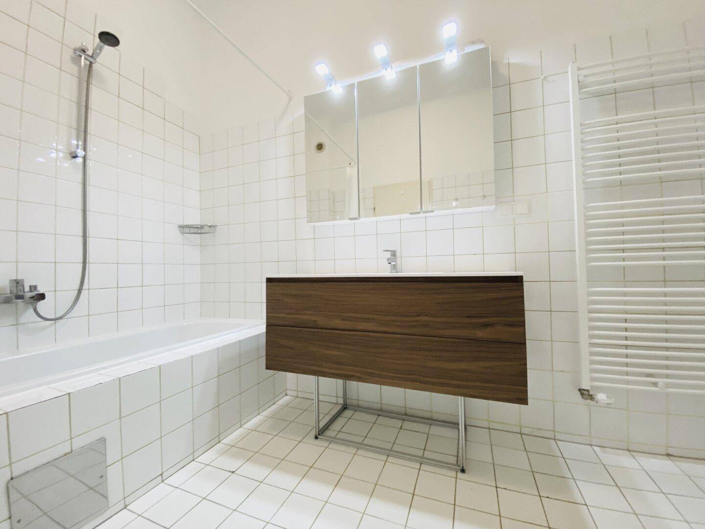 Helles Badezimmer mit Badewanne, Duschfunktion und einem modernen Waschtisch mit Spiegelschrank.