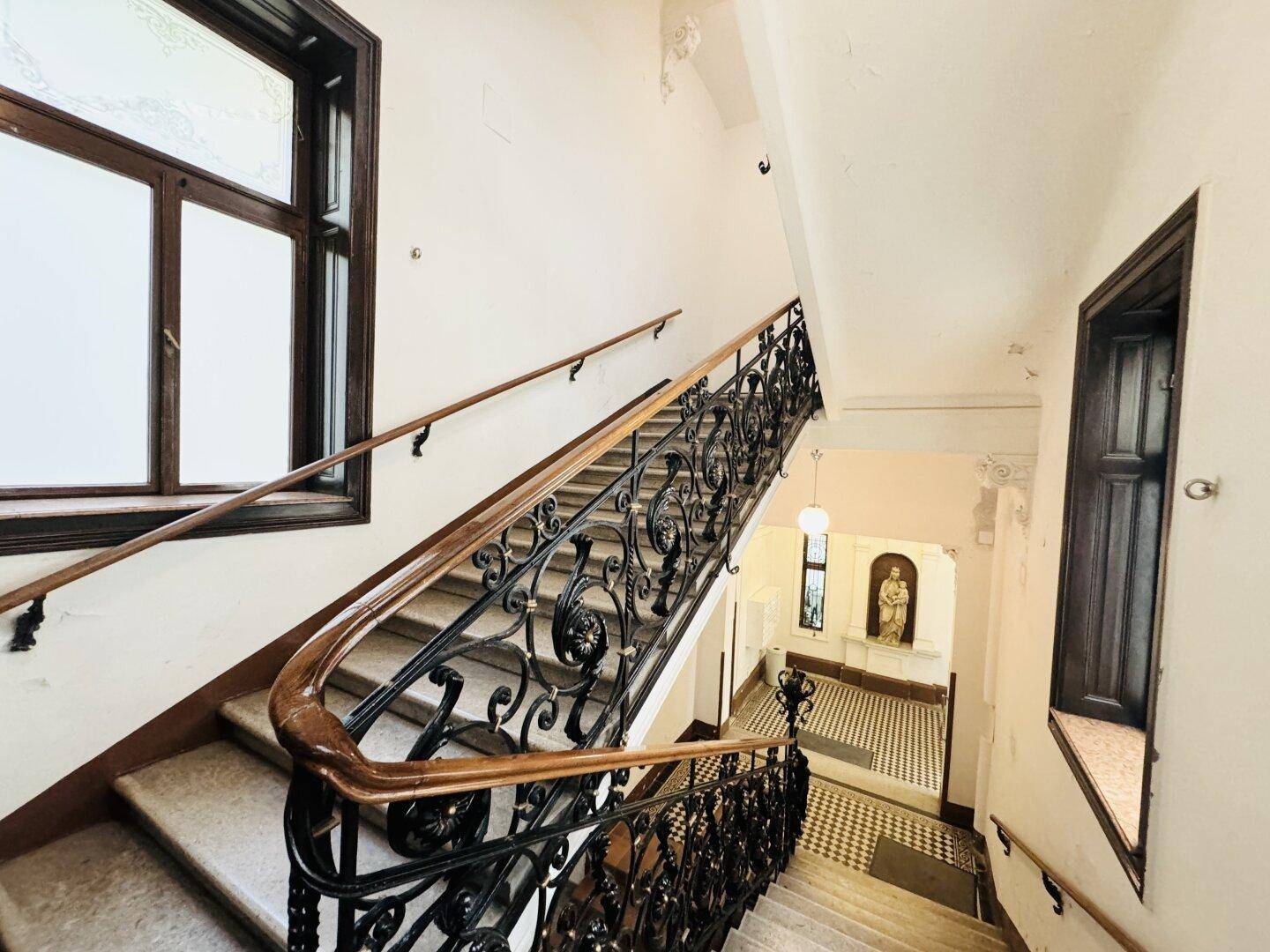 Elegantes Treppenhaus mit kunstvollem schmiedeeisernem Geländer, hohen Fenstern und historischem Charme.