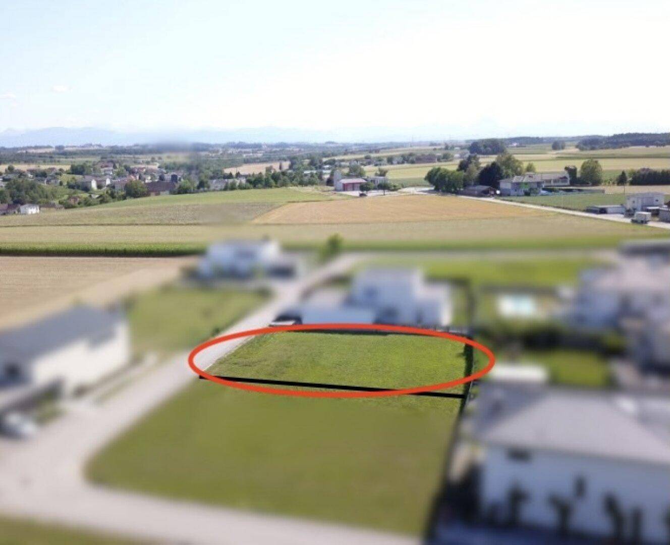 Weitläufige Luftaufnahme eines Baugrundstücks, umgeben von ländlicher Landschaft und weiteren Wohnhäusern.