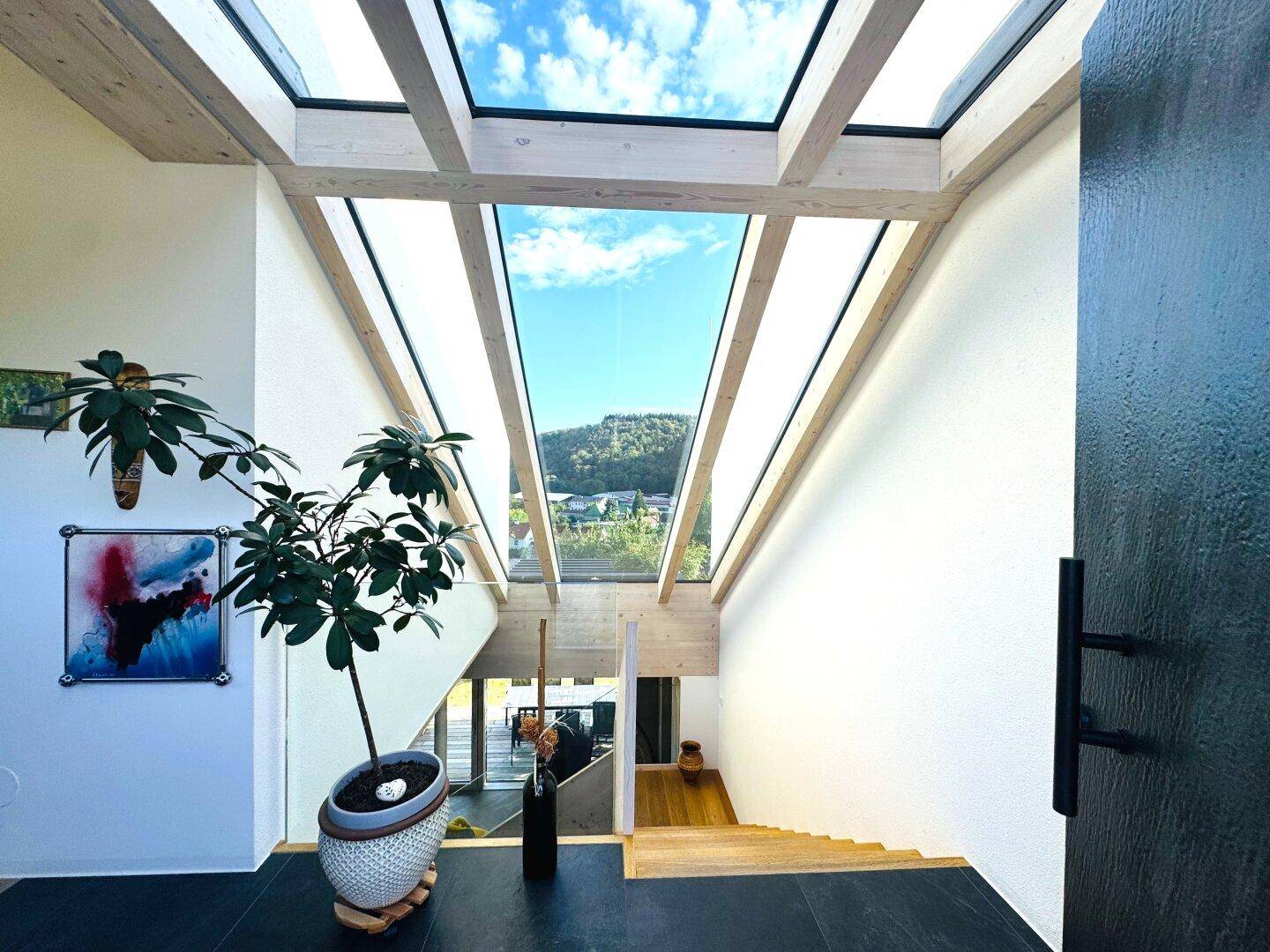 Heller Eingangsbereich mit hohen Decken, Holztreppe und großen Dachfenstern für viel Tageslicht.