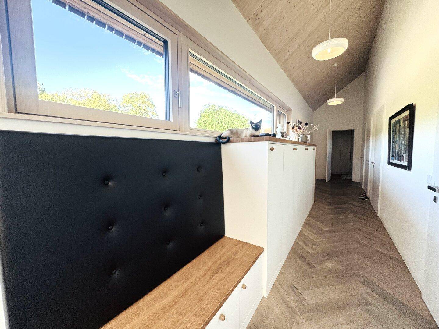 Langer Flur mit Holzparkett, eingebauter Sitzbank und Fenster für natürliches Licht.