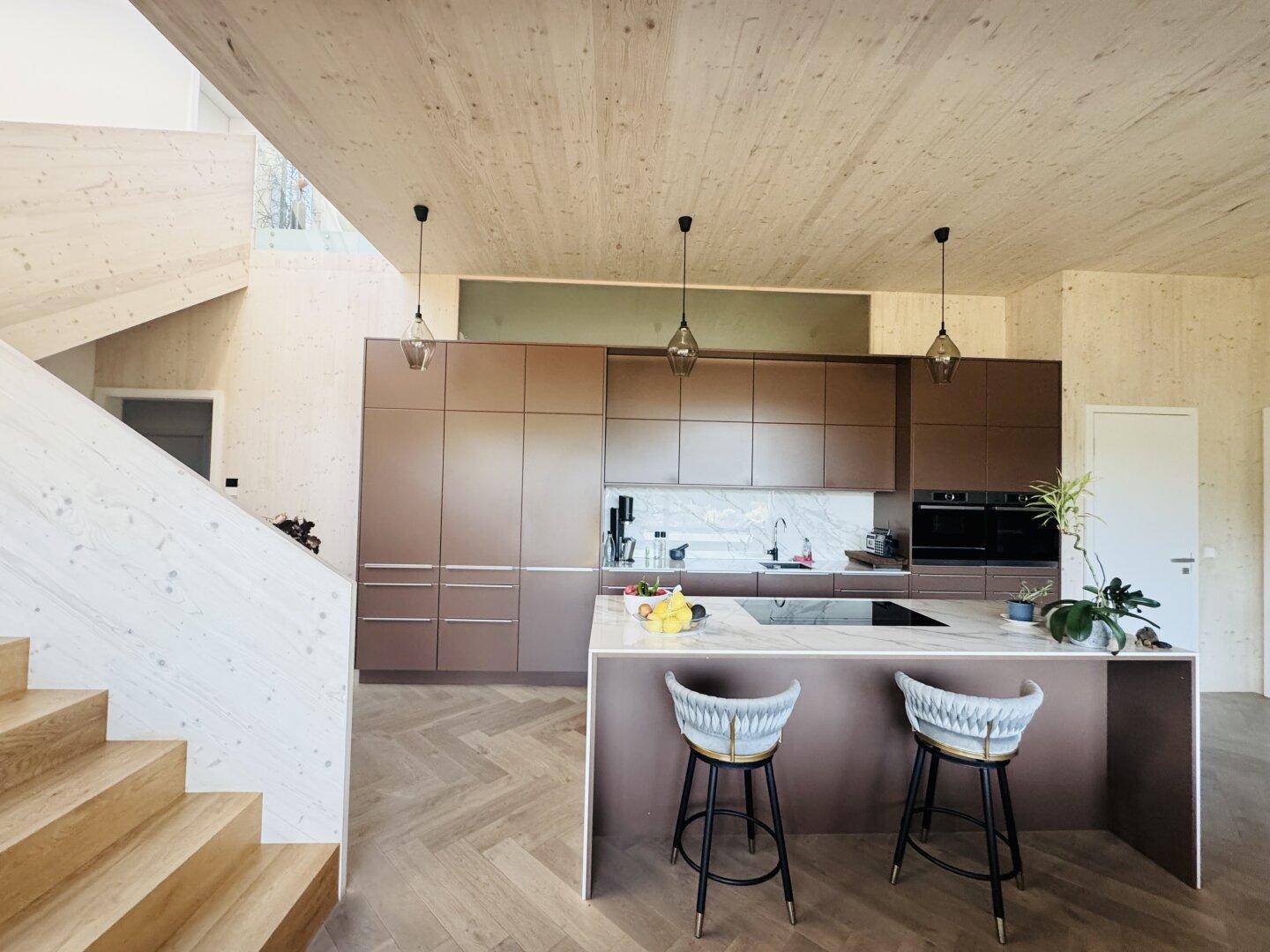 Moderne Einbauküche mit Kücheninsel, braunen Fronten und Holzboden in offenem Wohnkonzept.