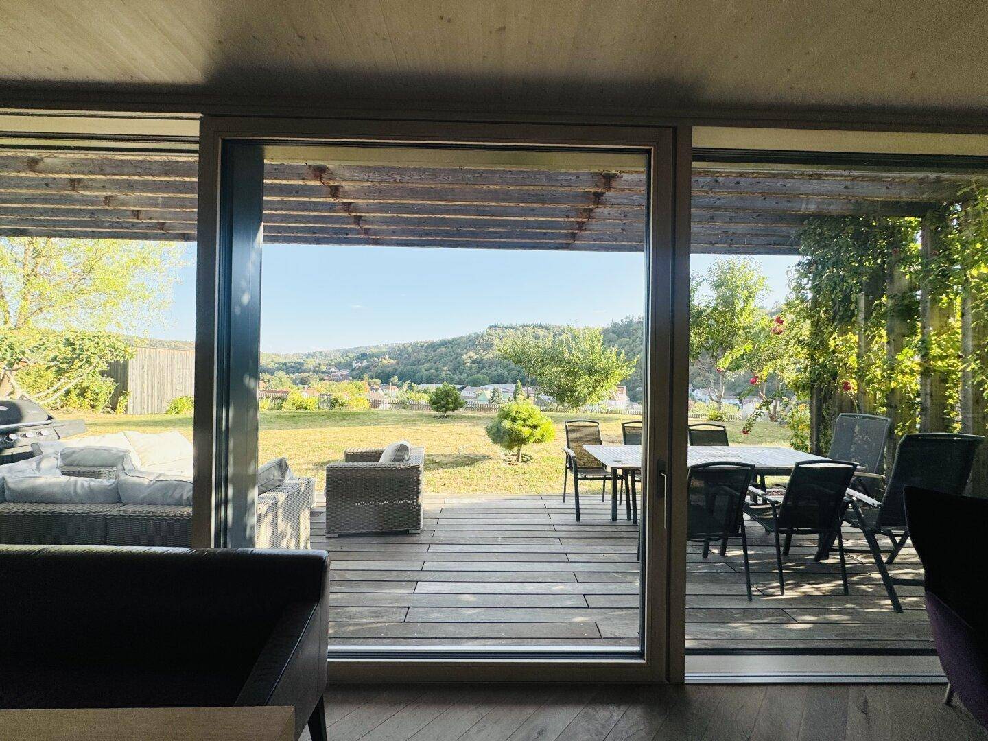 Heller Wohnbereich mit großen Schiebetüren, die zur Holzterrasse und in den Garten führen.