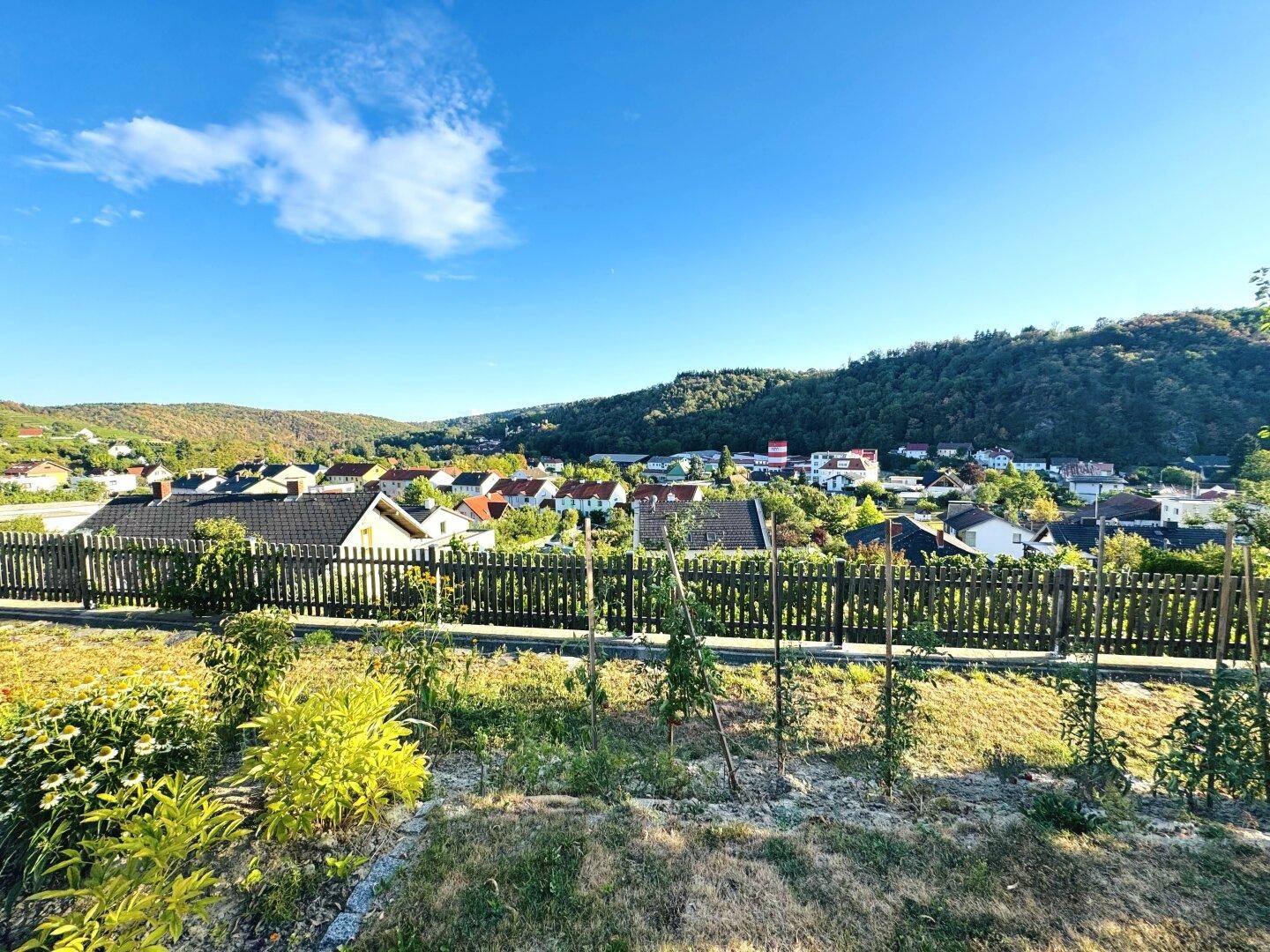 Panoramablick über eine malerische Siedlung und bewaldete Hügel unter blauem Himmel.