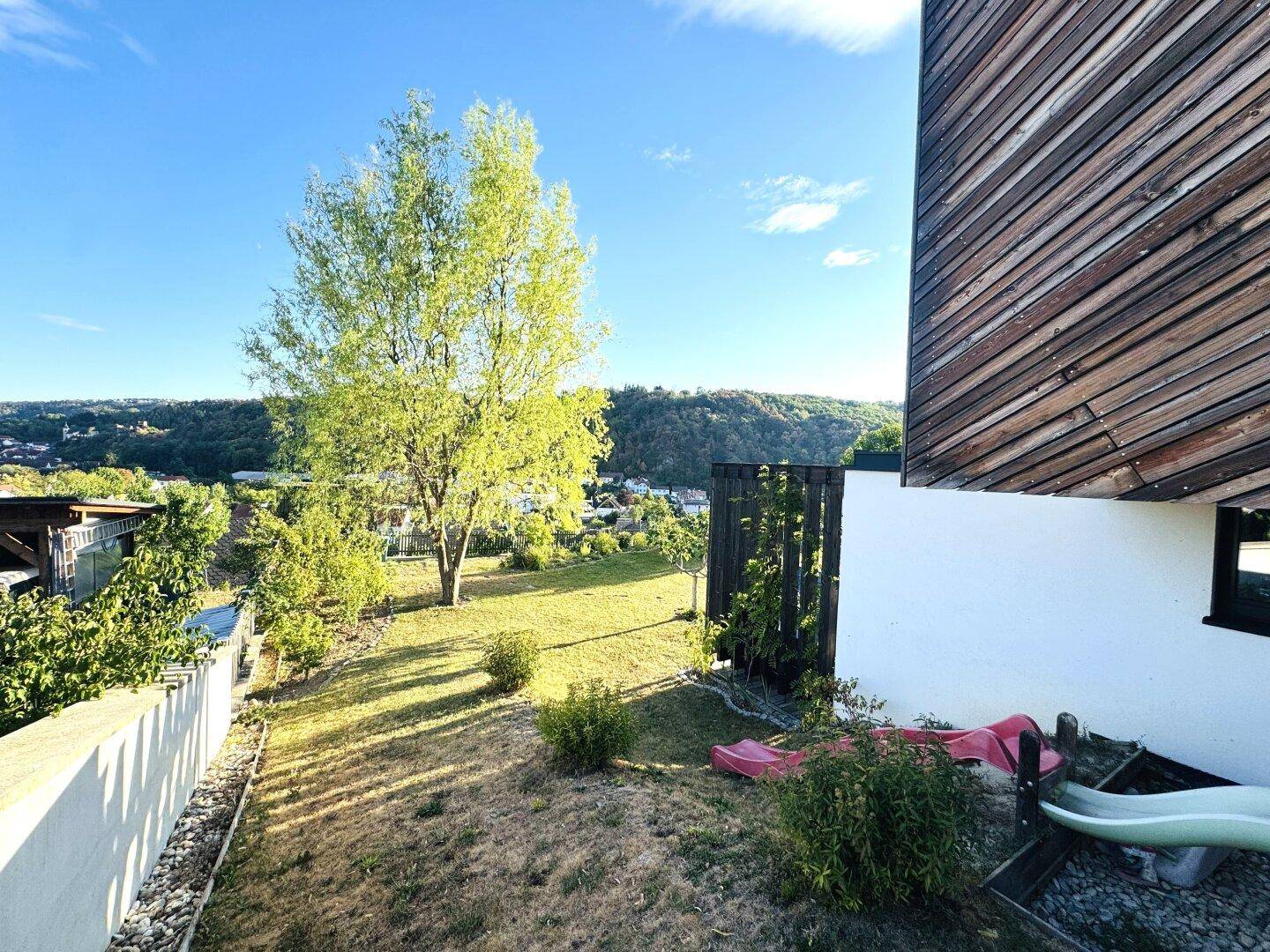 Grüner Gartenbereich mit Rasen, Bäumen und Blick auf die umliegende Landschaft.