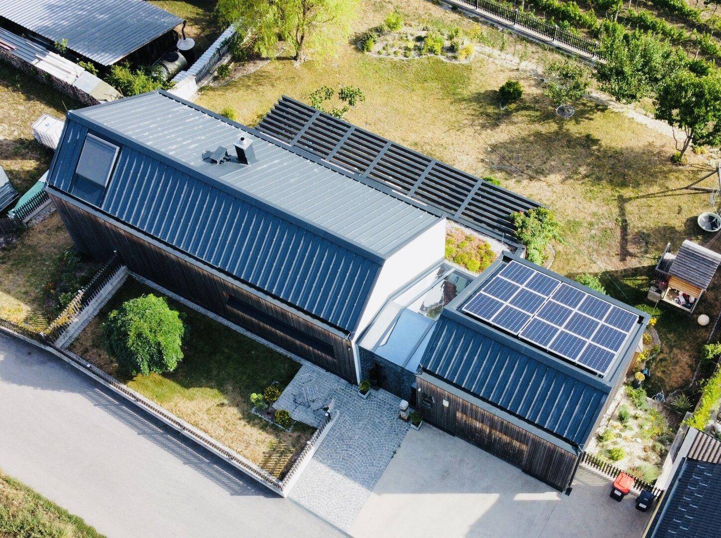 Luftaufnahme des modernen Hauses mit Holzfassade, Solaranlage und weitläufigem Grundstück.