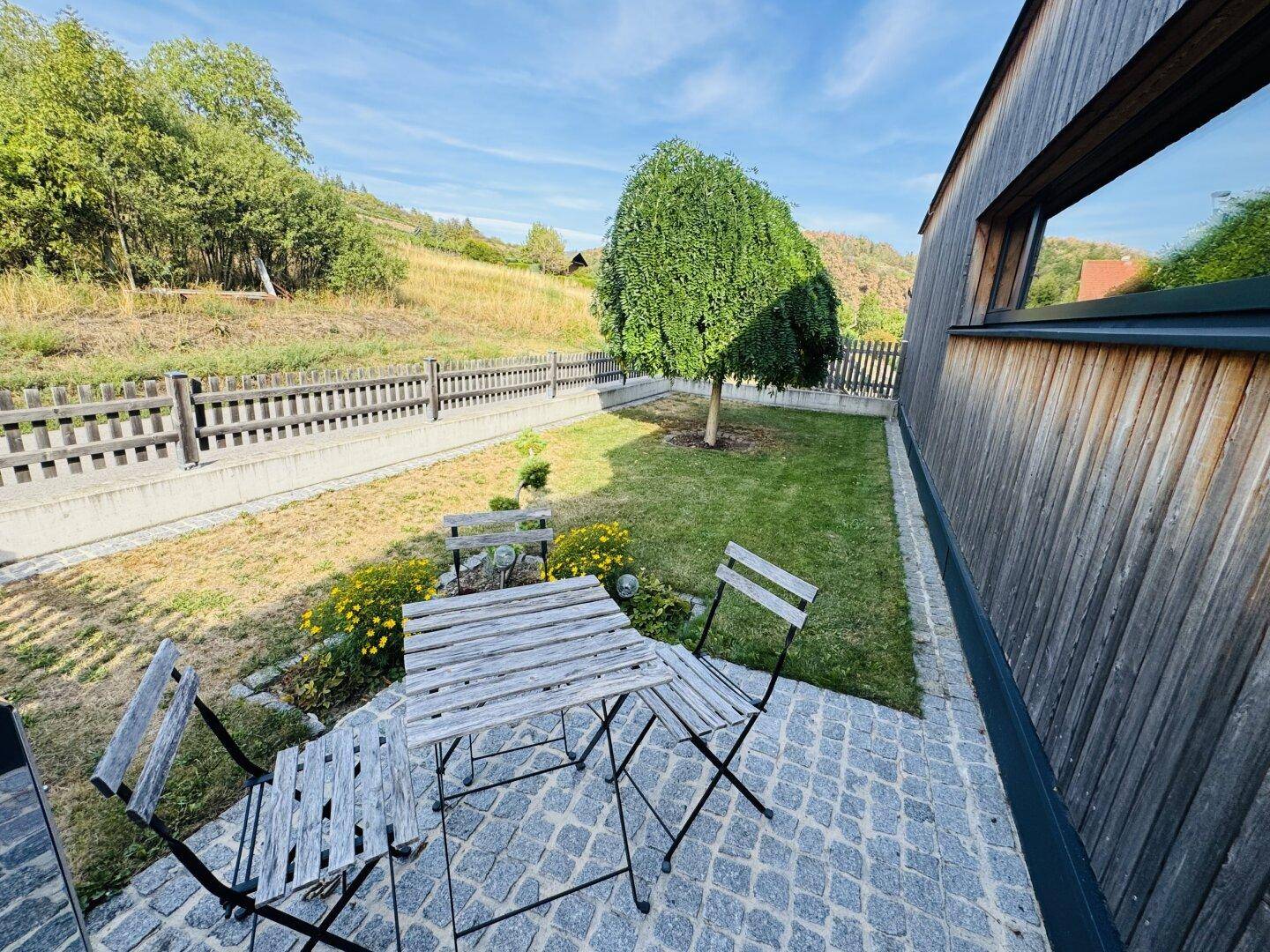 Kleine gepflasterte Terrasse mit Gartenmöbeln und Blick auf die grüne Umgebung.