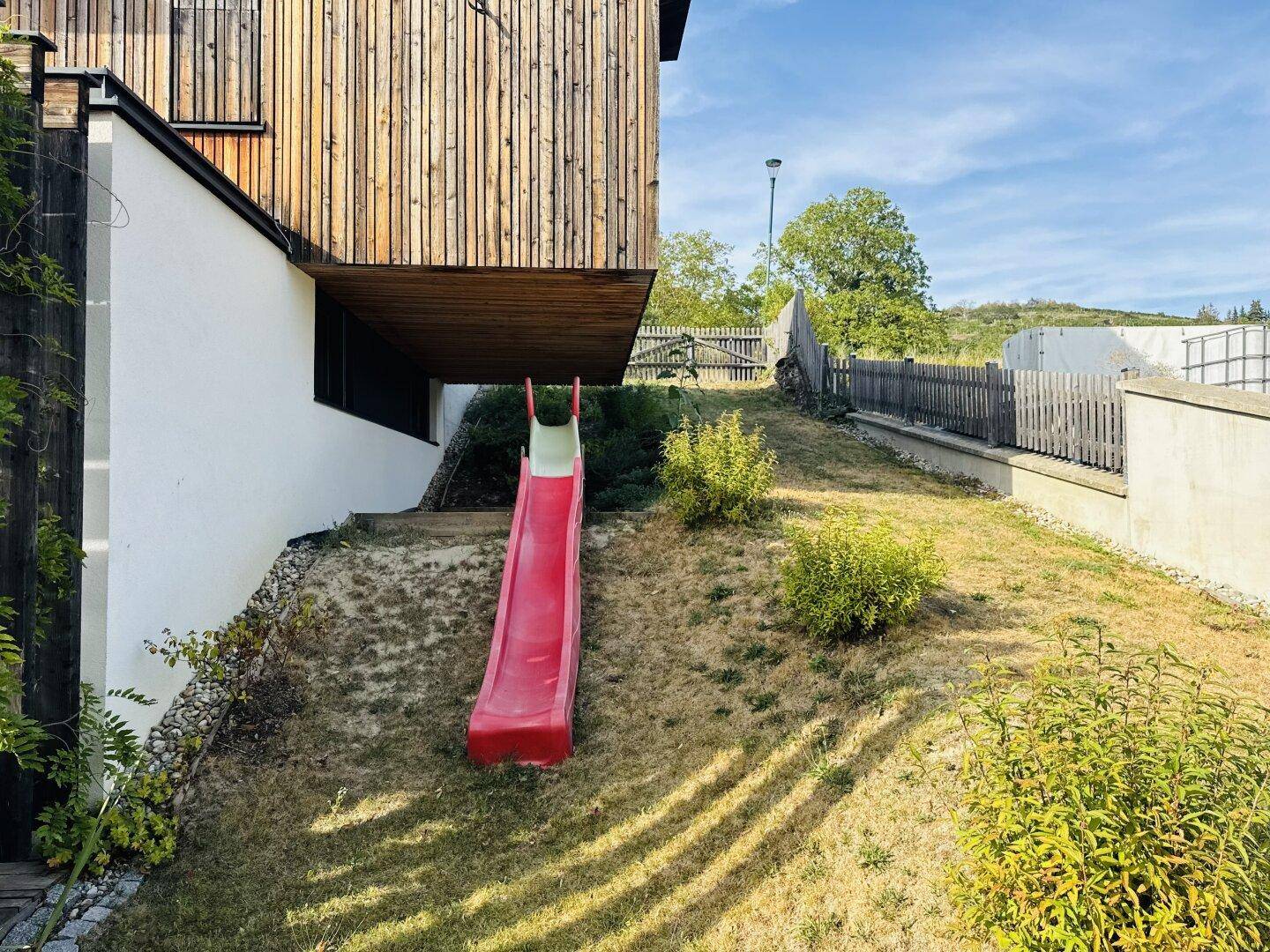 Kleiner roter Kinderrutsche im Gartenbereich neben dem Haus.