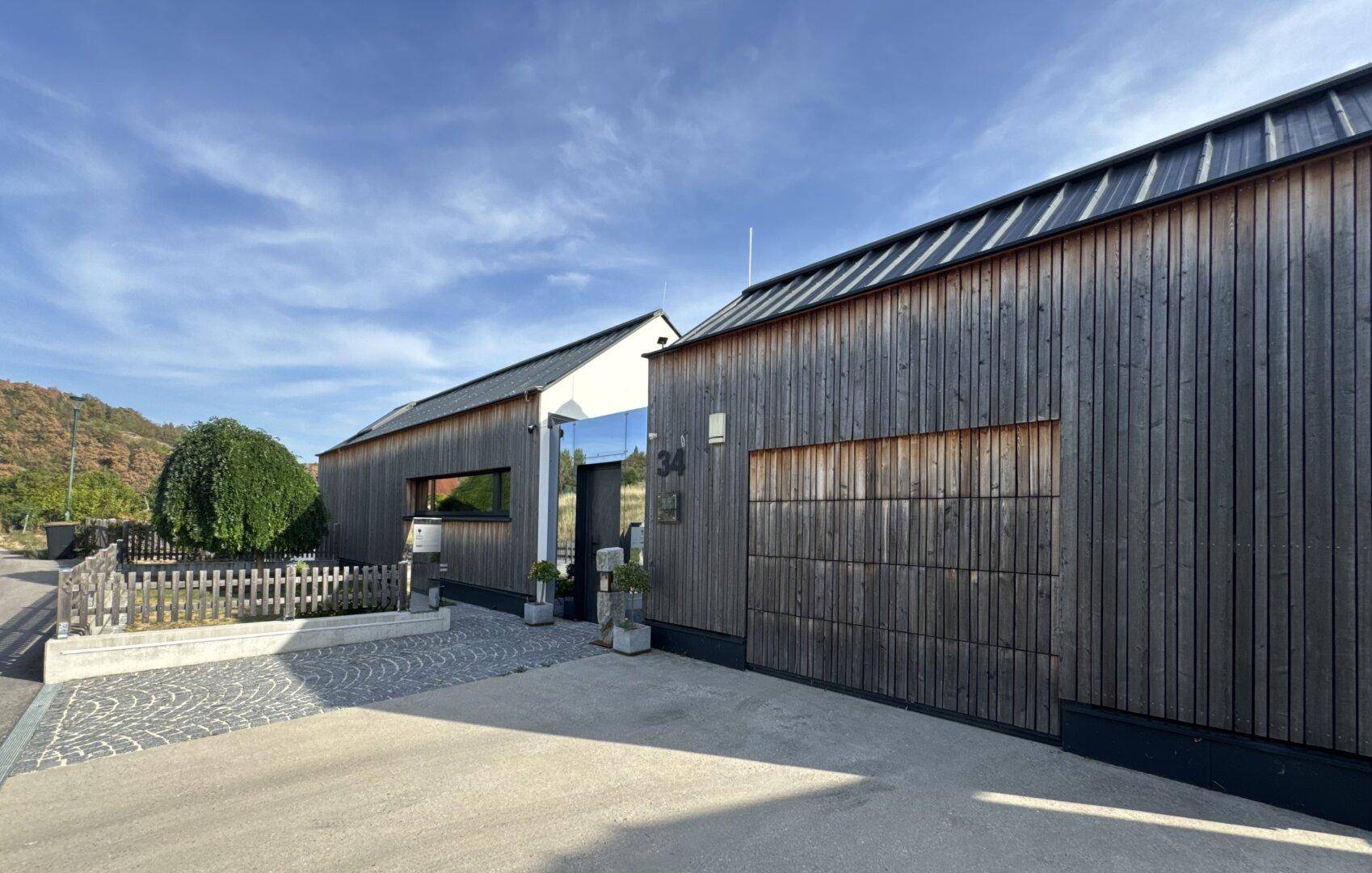 Moderne Holzfassade des Hauses mit Eingangsbereich und Garagentor unter klarem Himmel.