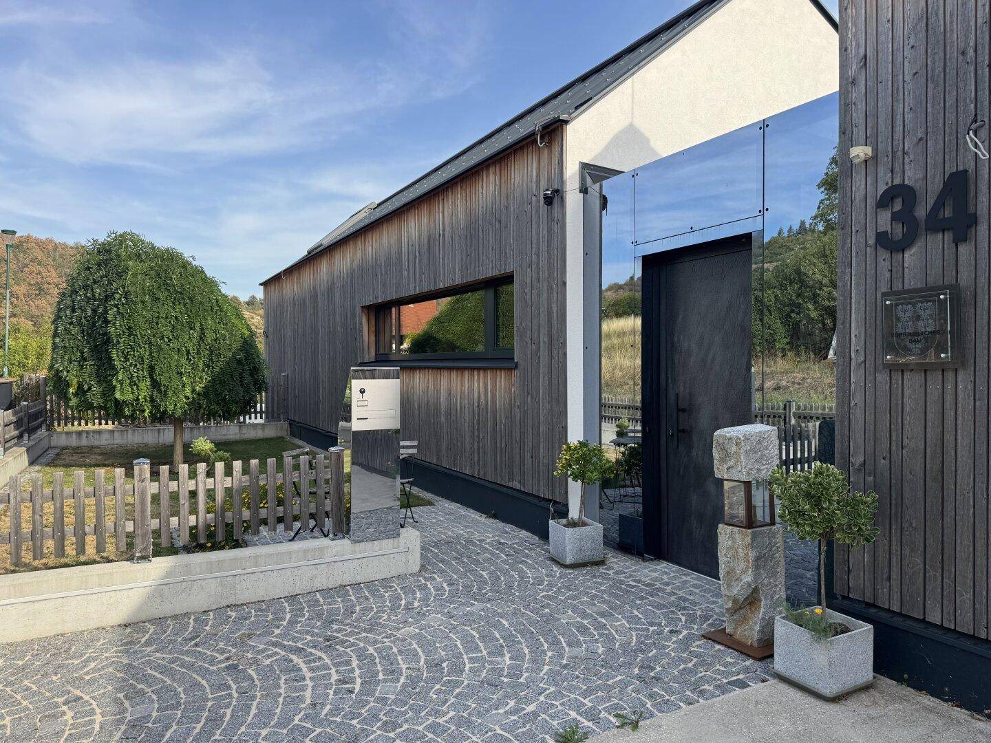 Moderner Eingangsbereich mit Holzfassade, gepflastertem Weg und Hausnummer 34.
