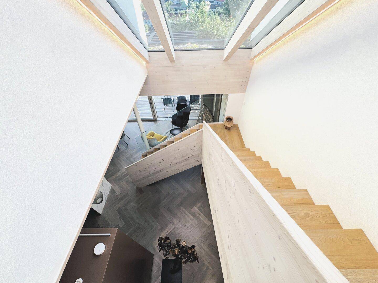 Offener Wohnbereich mit Holztreppe, hohen Decken und viel Tageslicht durch große Fenster.