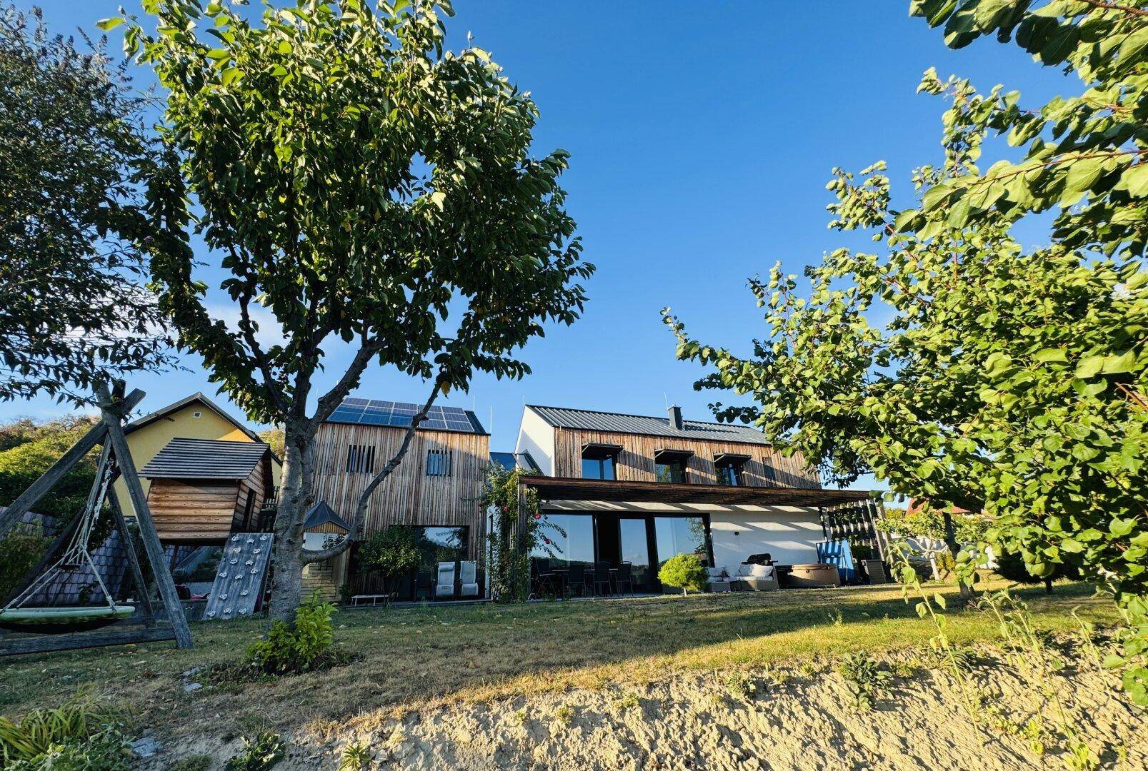 Modernes Haus mit Holzfassade, großem Garten und Schaukelbereich für Kinder.