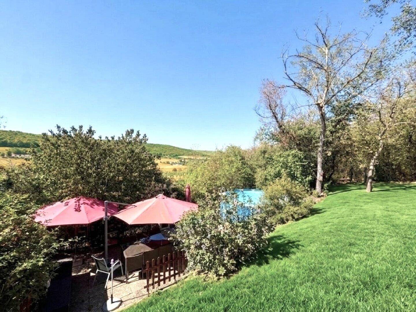 Gemütlicher Außenbereich mit roten Sonnenschirmen und Sitzgelegenheiten, umgeben von üppigem Grün und Fernblick.