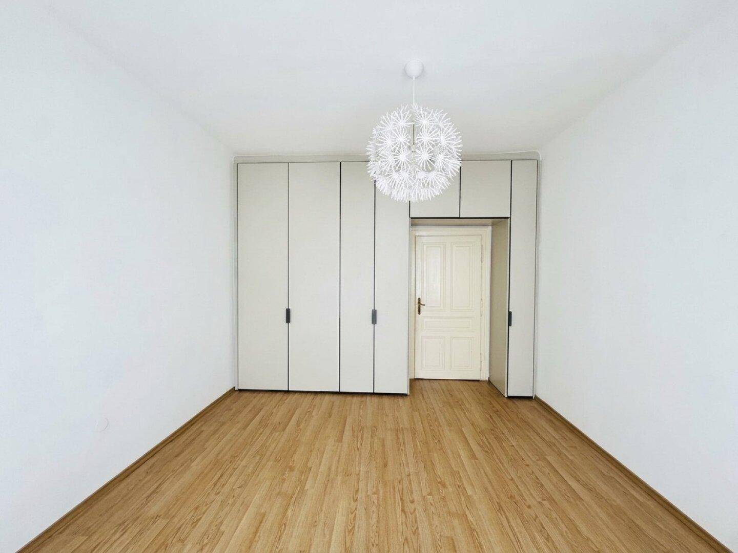 Schlafzimmer mit integrierten Kleiderschränken, Holzboden und einer modernen Deckenleuchte.