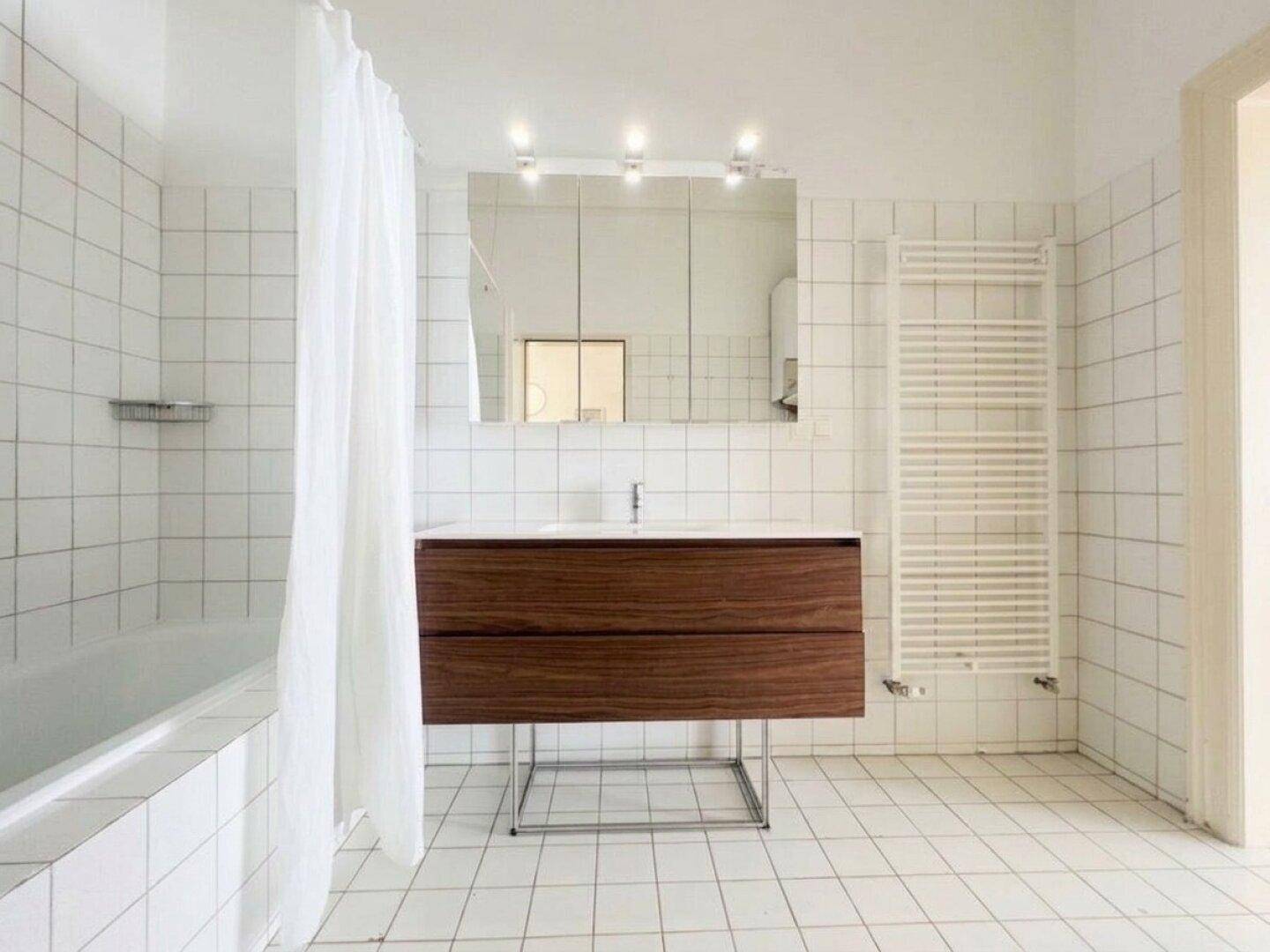 Modernes Badezimmer mit weißen Fliesen, Holzwaschtisch, Badewanne und beheiztem Handtuchhalter.