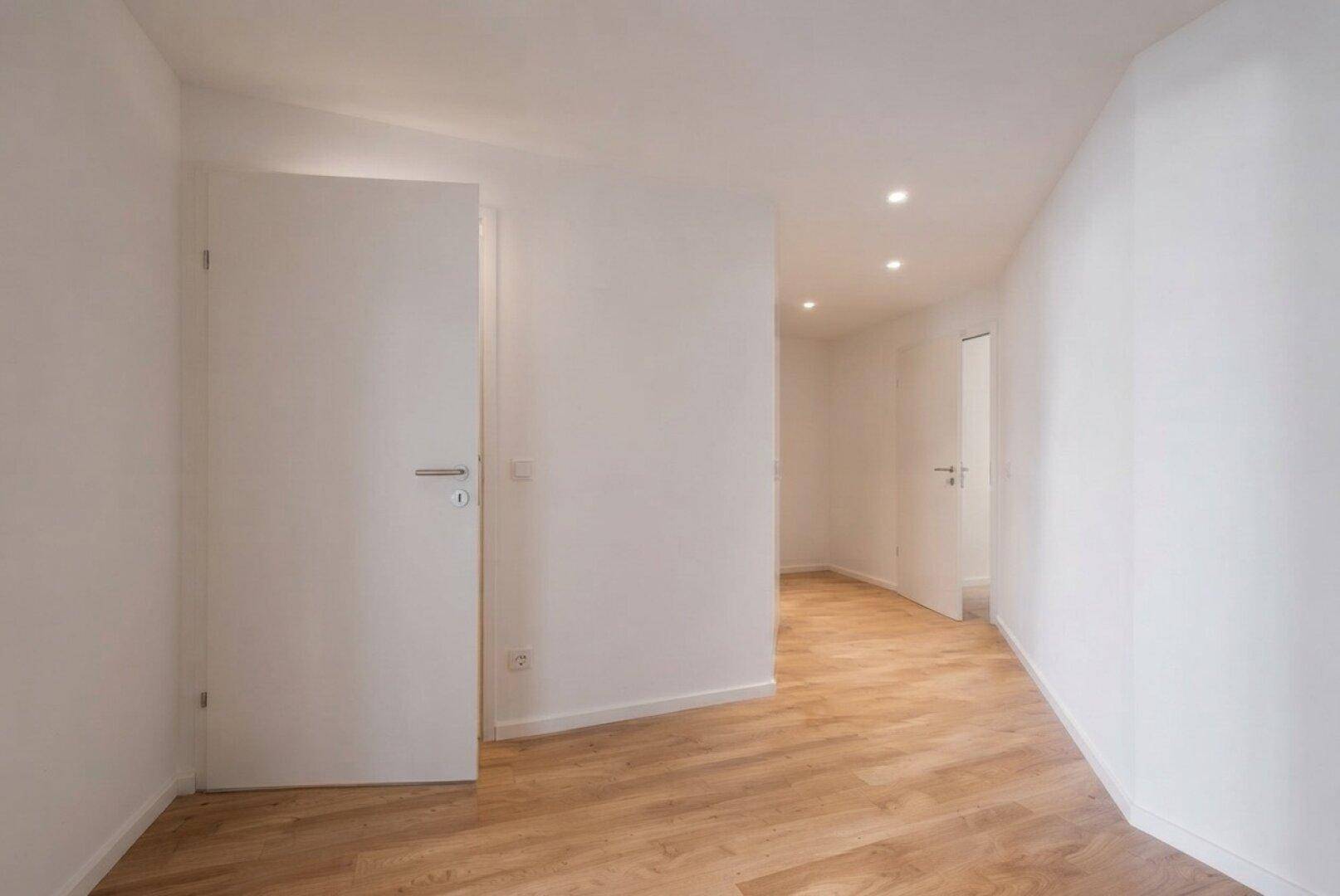Heller Flur mit Laminatboden, weißen Wänden und integrierten Deckenspots.