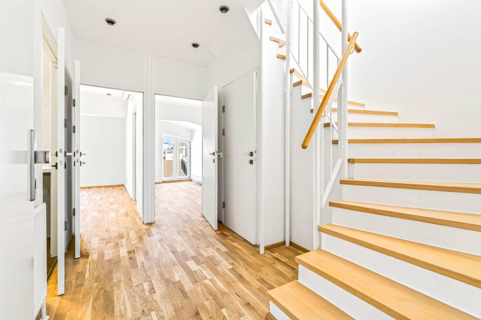 Heller Flur mit Holztreppe, Holzboden und Zugang zu weiteren Räumen.