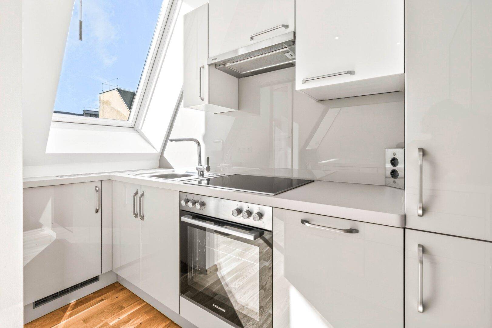 Moderne weiße Einbauküche mit Induktionskochfeld, Backofen und Dachfenster.