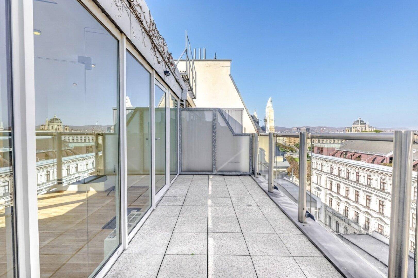Lange Terrasse mit Glasgeländer und Panoramablick auf die Stadt und historische Gebäude.