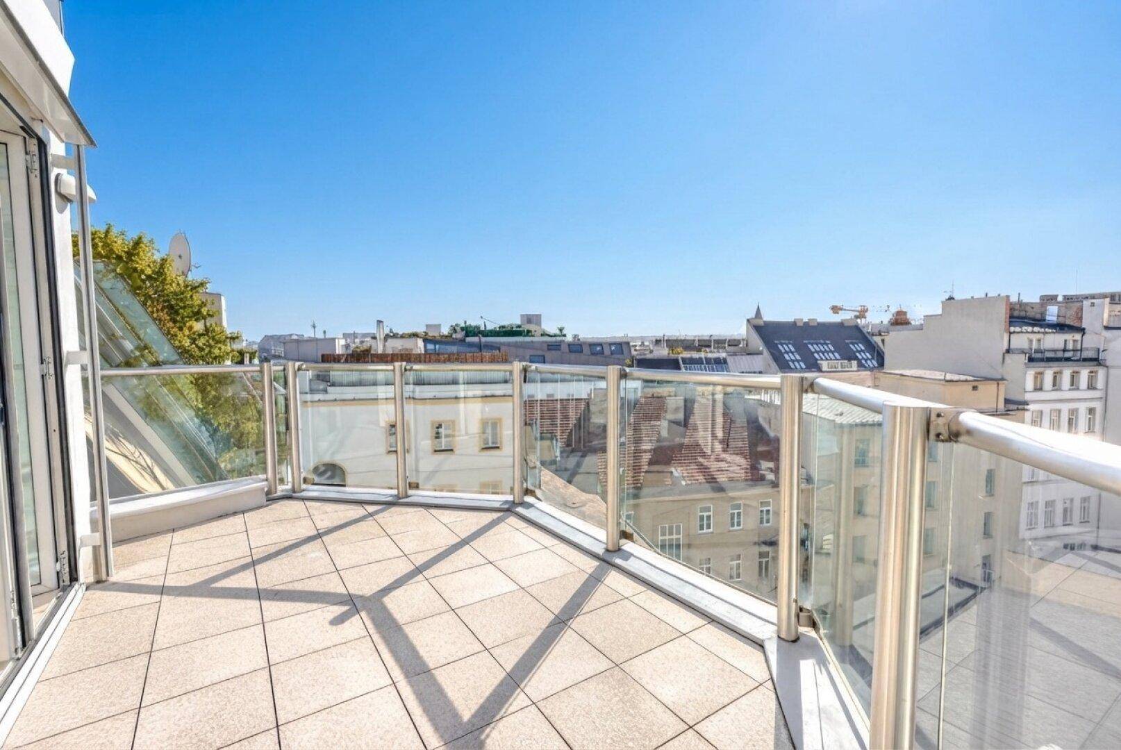 Geräumiger Balkon mit Glasgeländer und weitem Blick über die Dächer der Stadt.