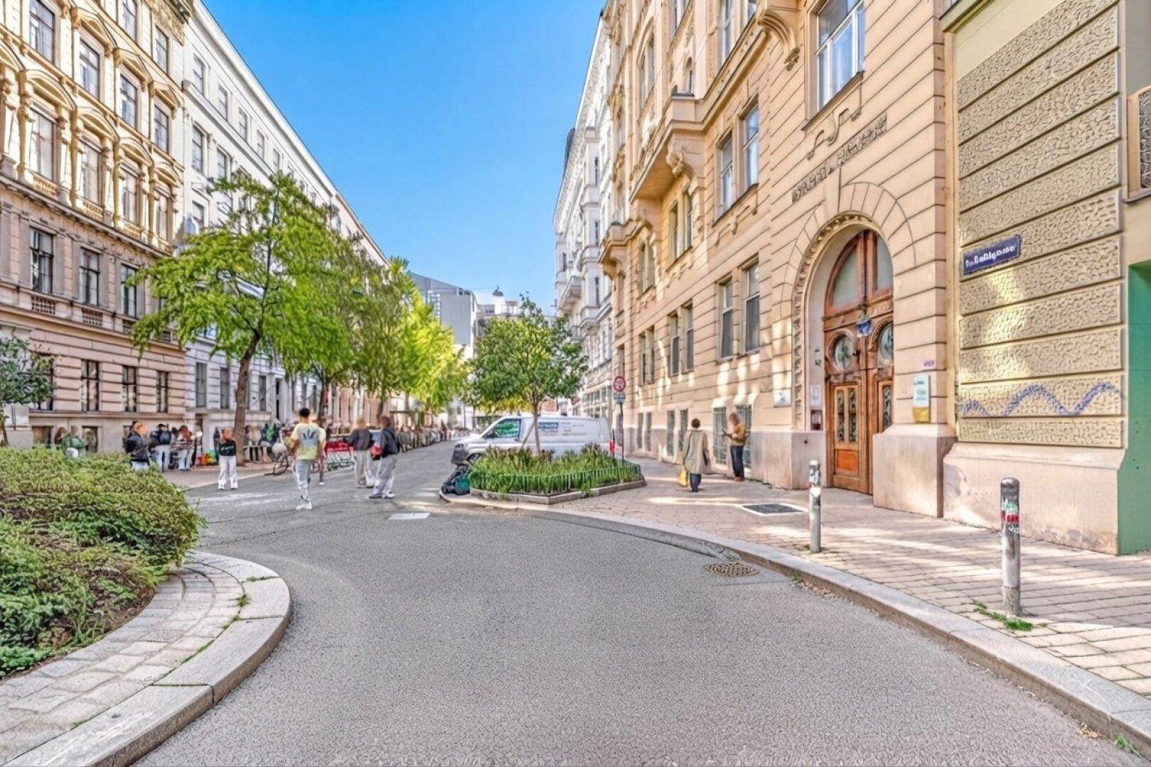 Ruhige Stadtstraße mit Bäumen, historischen Gebäuden und Fußgängern an einem sonnigen Tag.