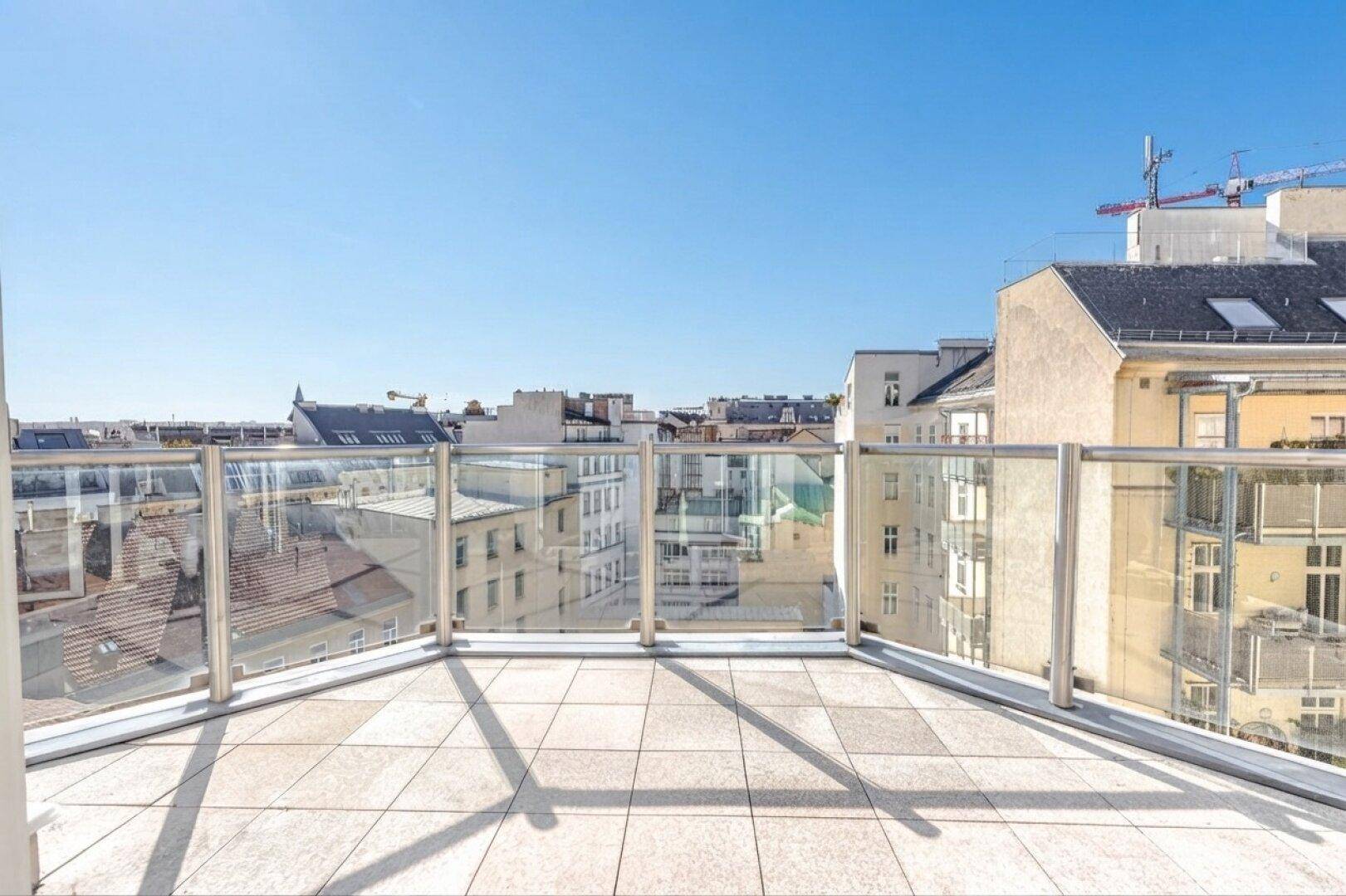 Geräumiger Balkon mit Glasgeländer und weitem Blick über die Dächer der Stadt.